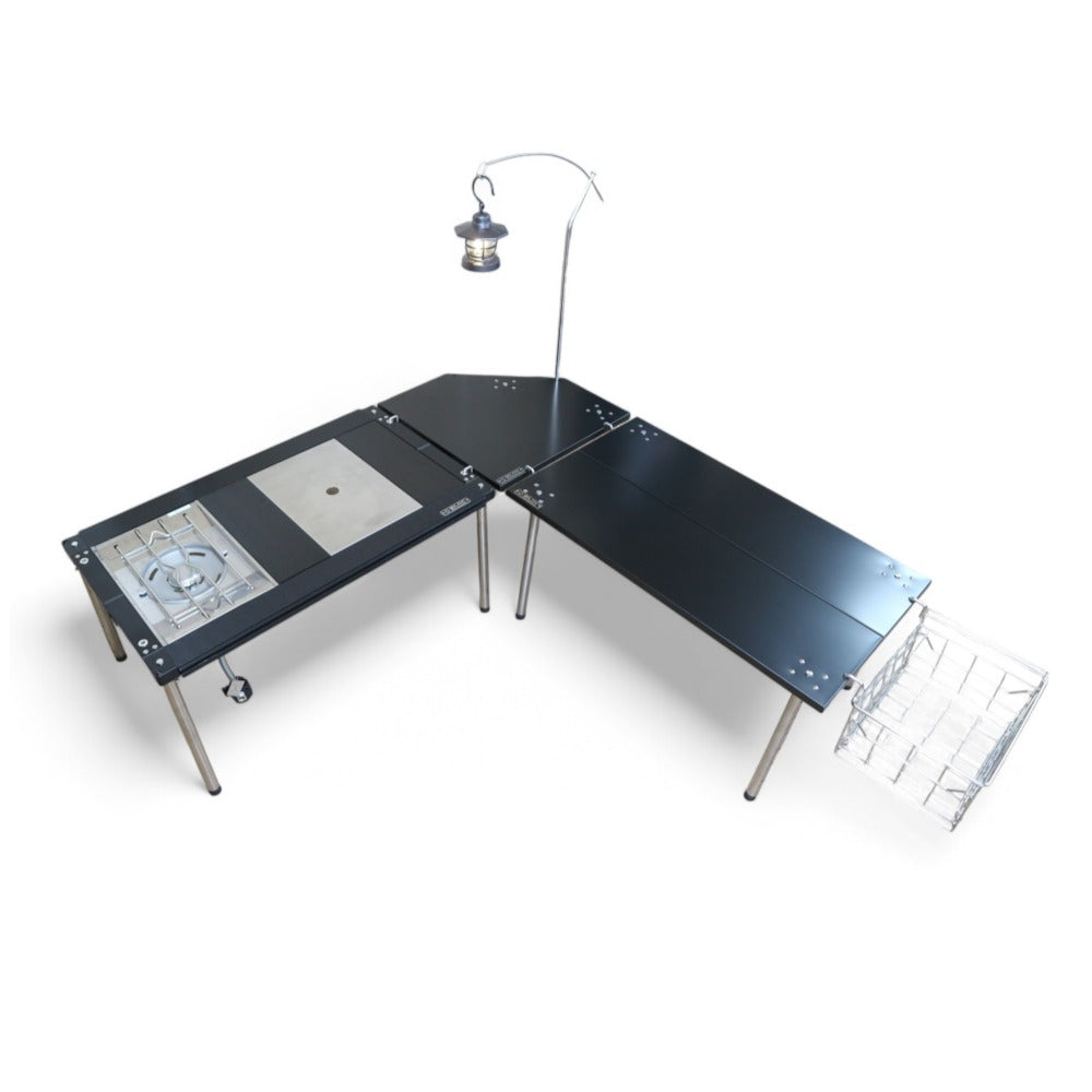 L-shaped camp kitchen made of two IGT tables joined by the black corner table, with a lantern arm and wire basket mounted. The tables, lantern and basket are separate purchases.