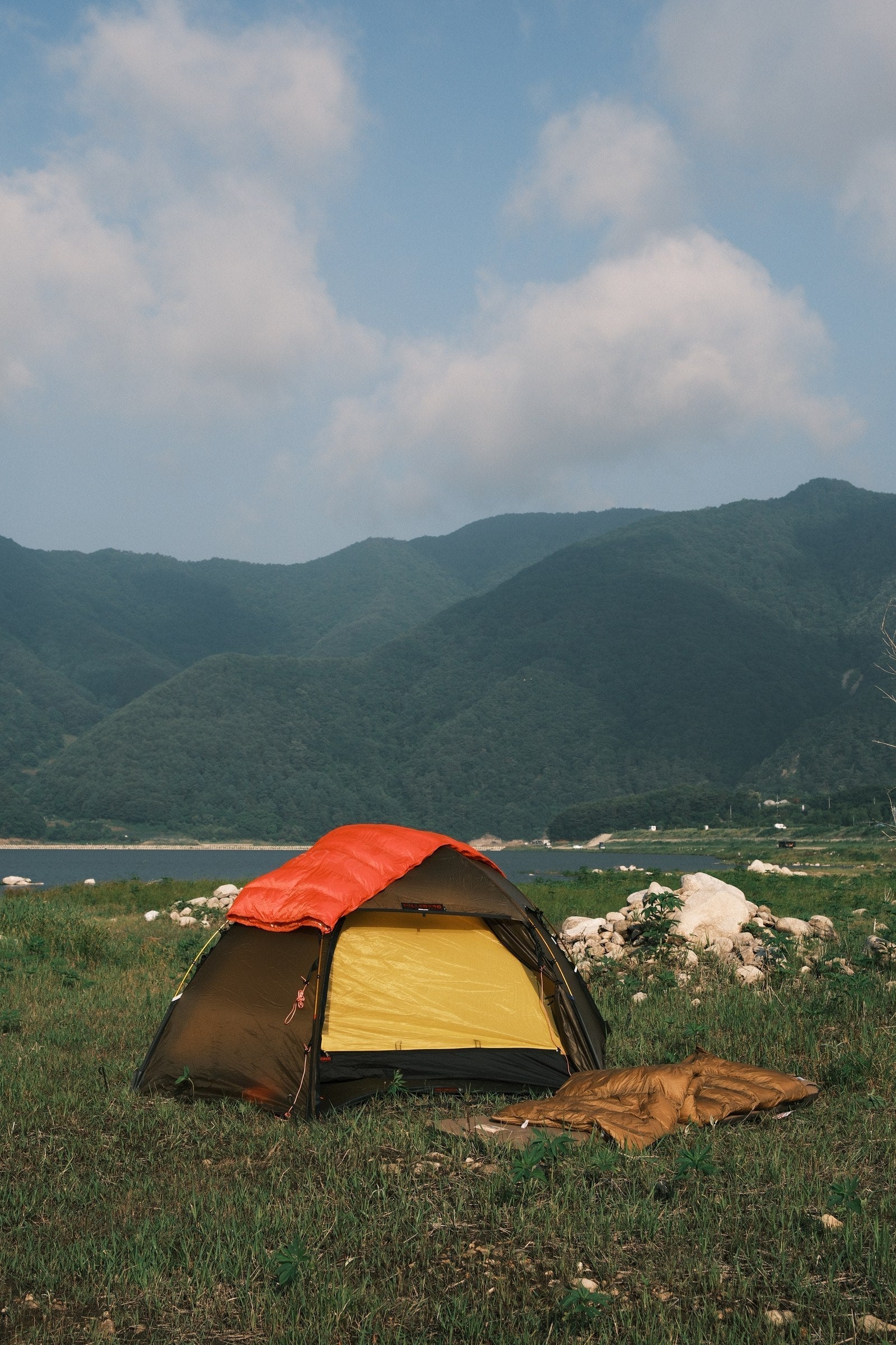 Orange DEOS camp comforter in a tent by the river at dusk