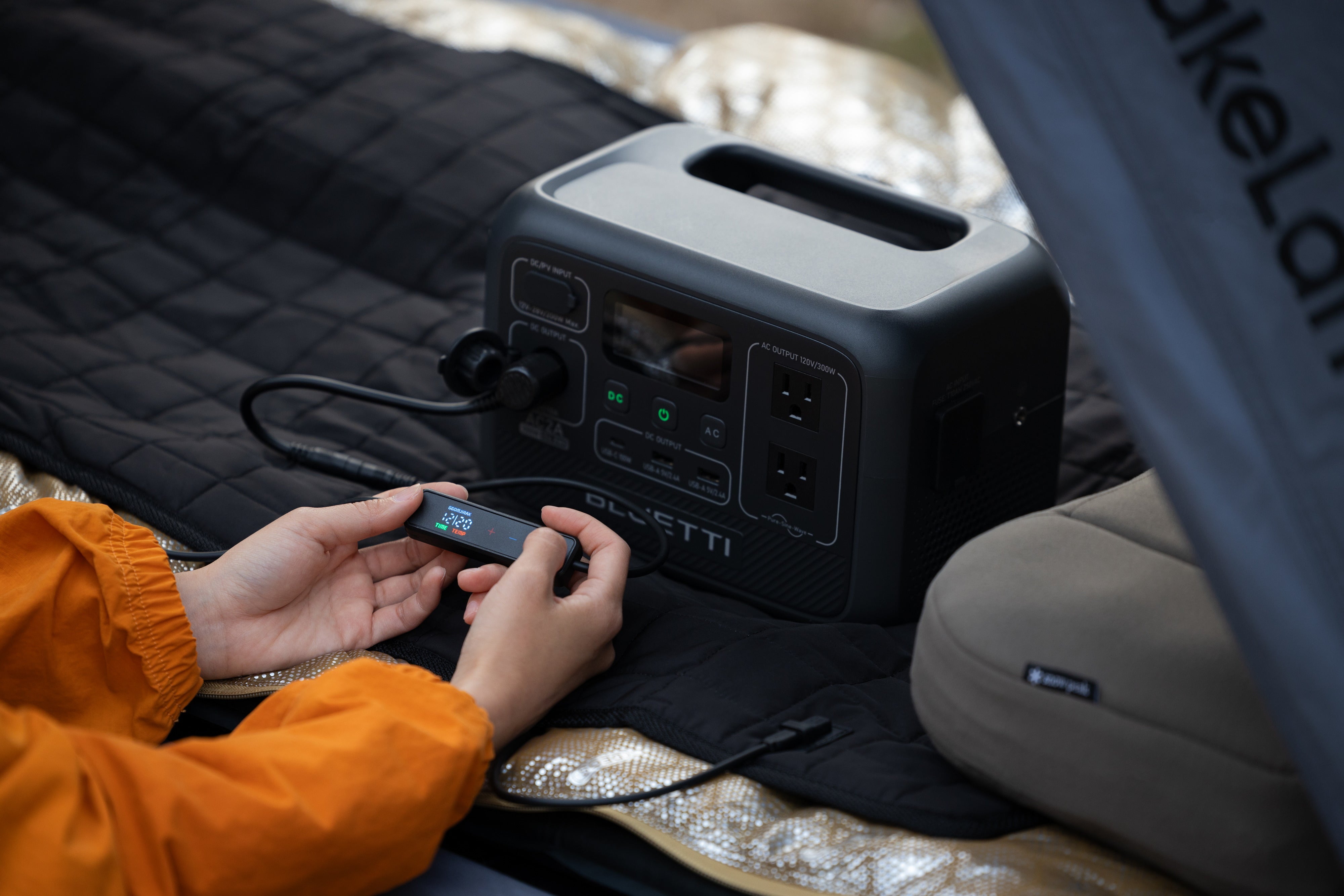 Hands adjusting the Carbon Heating Pad Large controller, with the pad's 12V adapter plugged into the DC output of a portable power station.