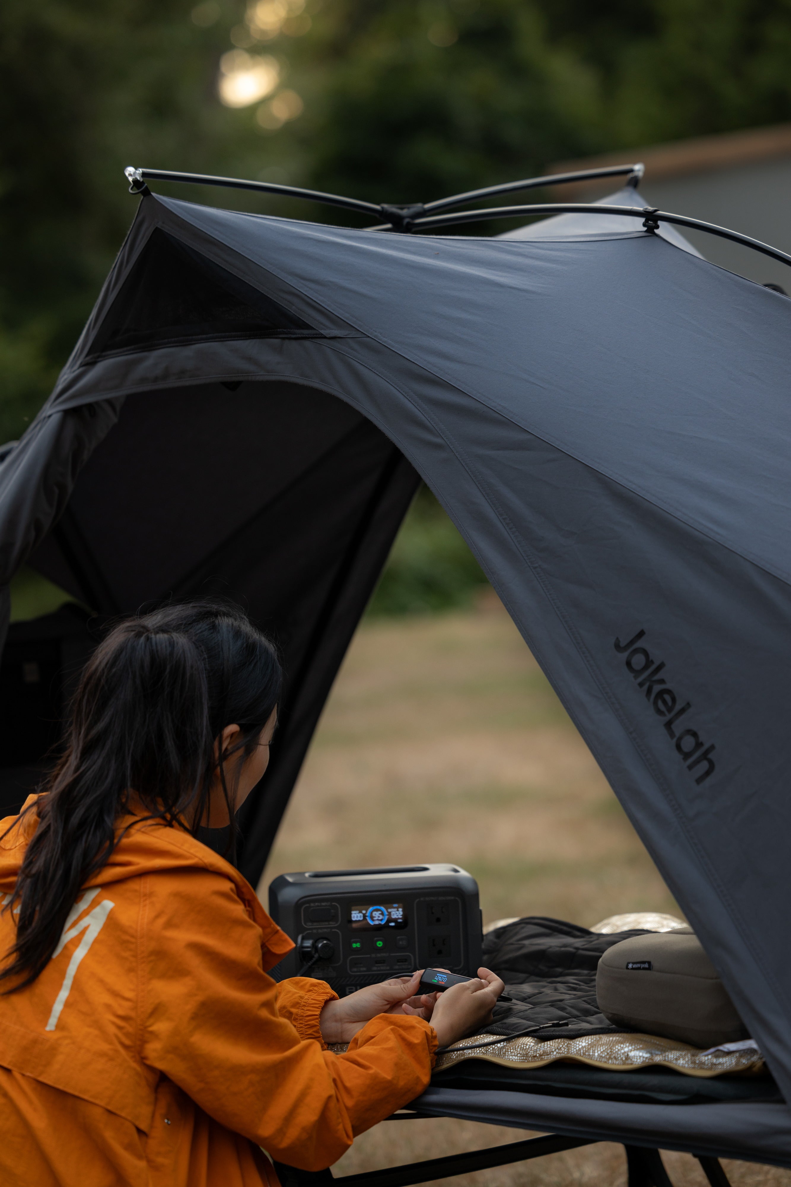 The Carbon Heating Pad Large laid flat on a camp cot inside an open shelter, connected by cable to a portable power station.