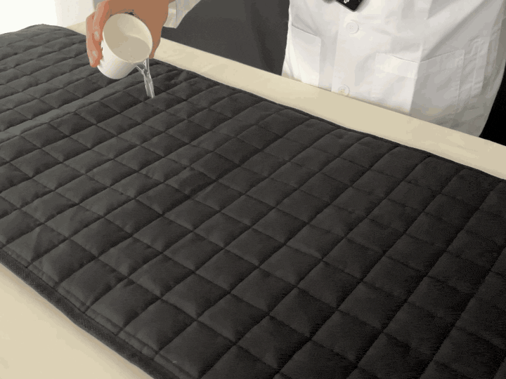 Water poured onto the heating pad beading and rolling off the water-repellent fabric
