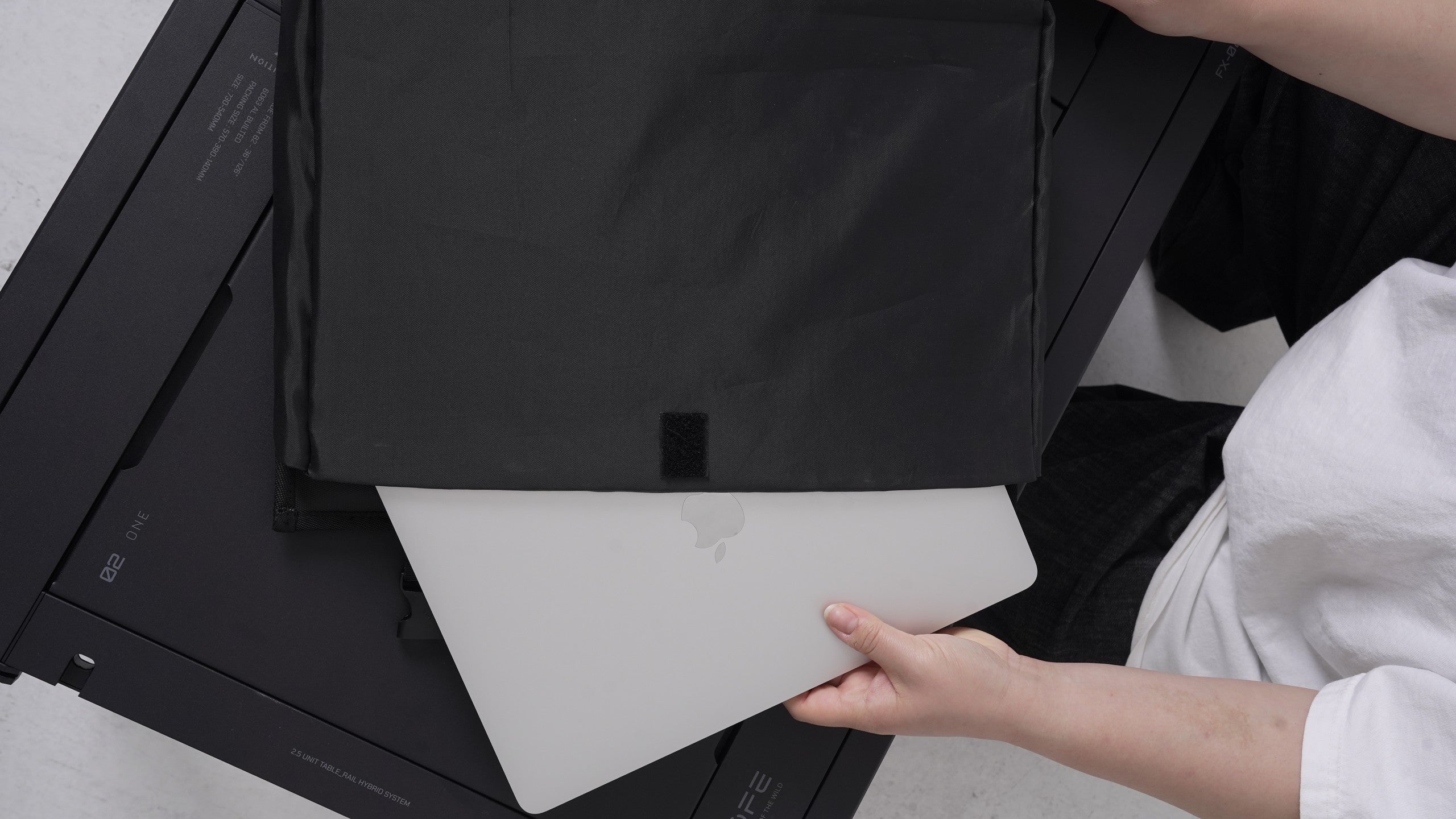 BUENOFE Multi Storage Bag Slim with a silver laptop being slid into its flat main compartment, demonstrating that the slim bag holds notebooks and tablets, photographed over a dark modular camp table.