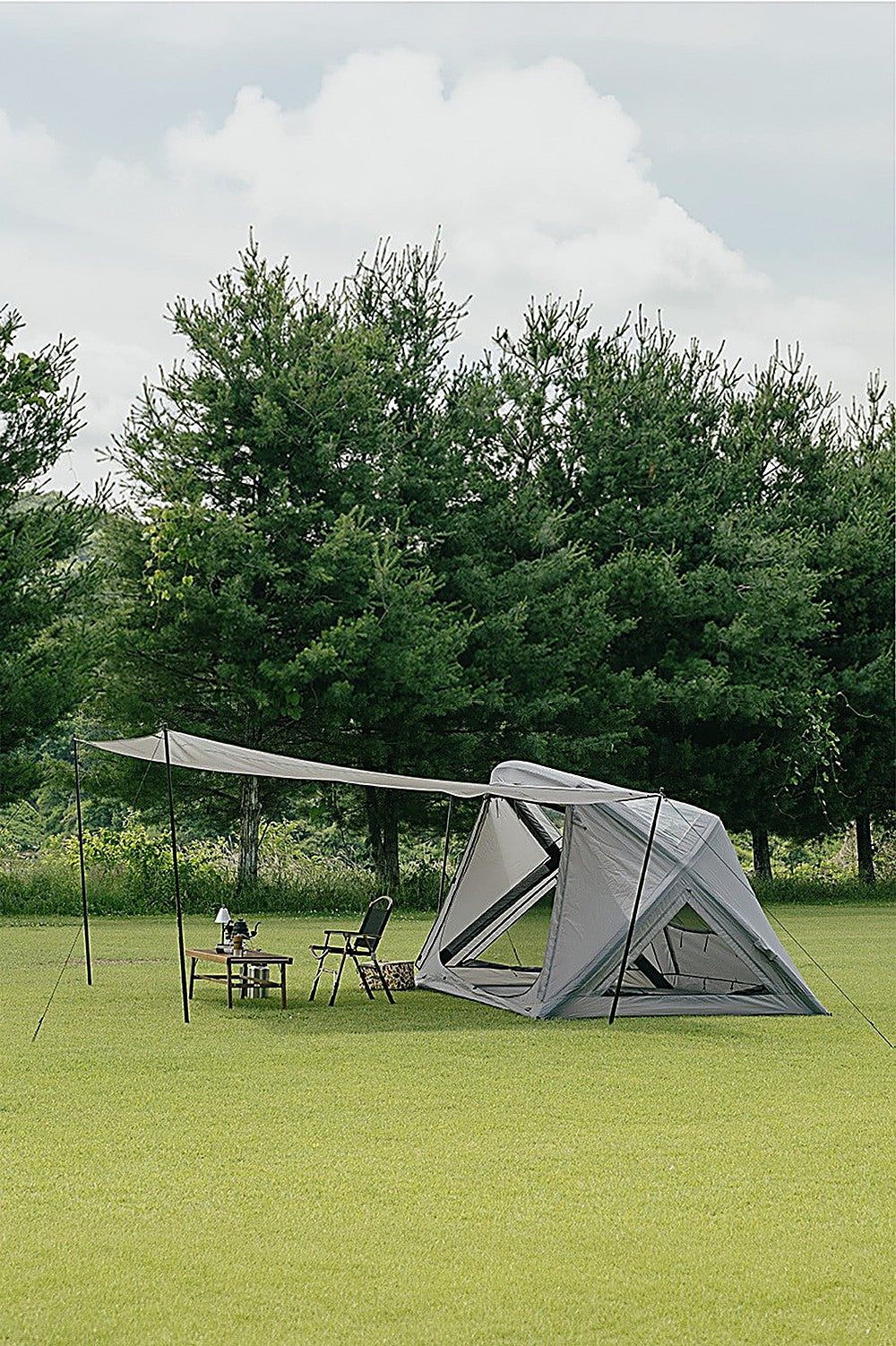Side view of the GEO AIR4 Extension Sun Shade shading a folding chair and camp table beside the tent, pine trees behind
