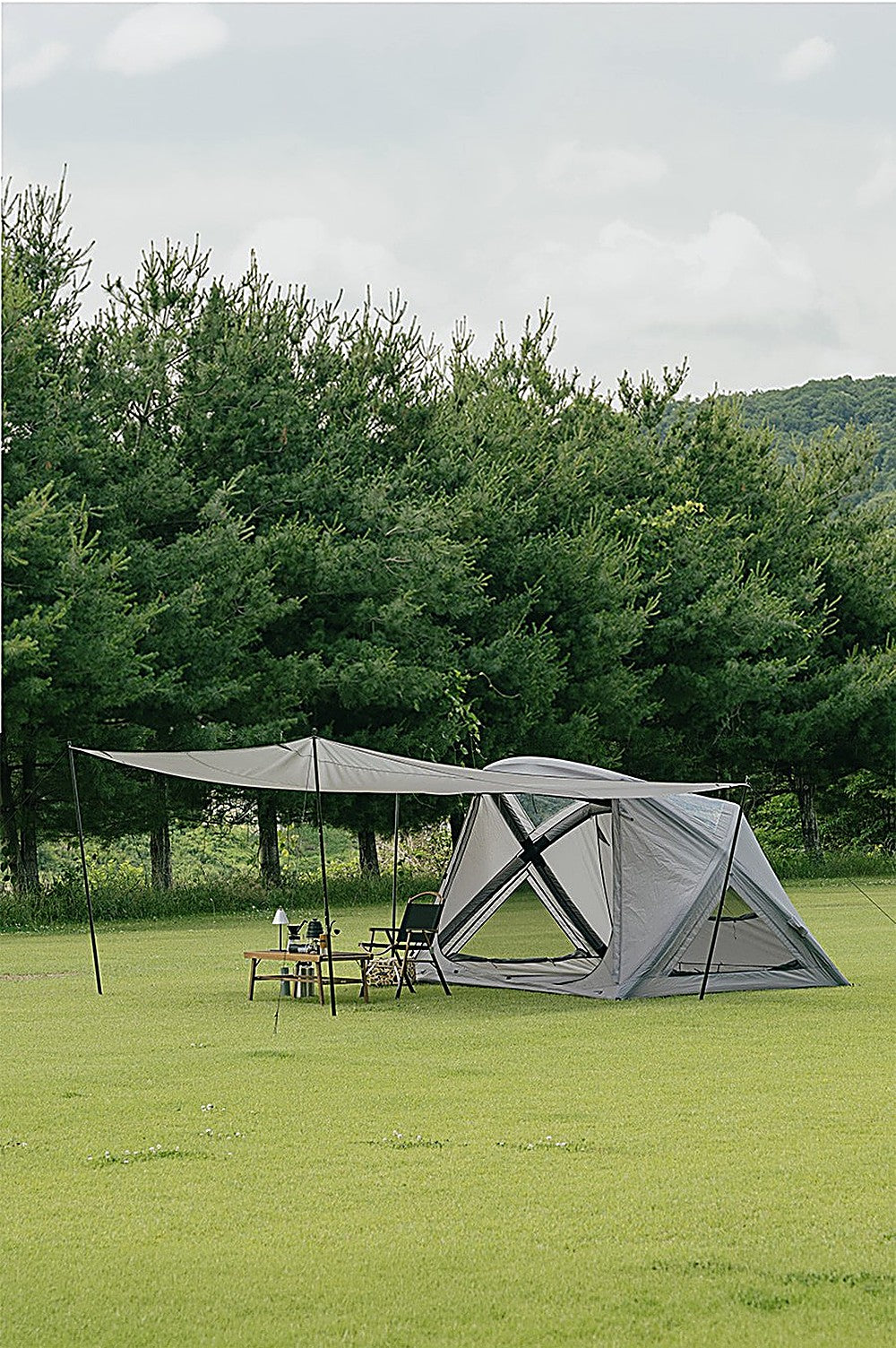 GEO AIR4 air tent with Extension Sun Shade awning over a lamp-lit camp table on a wide lawn, crossed mesh window visible