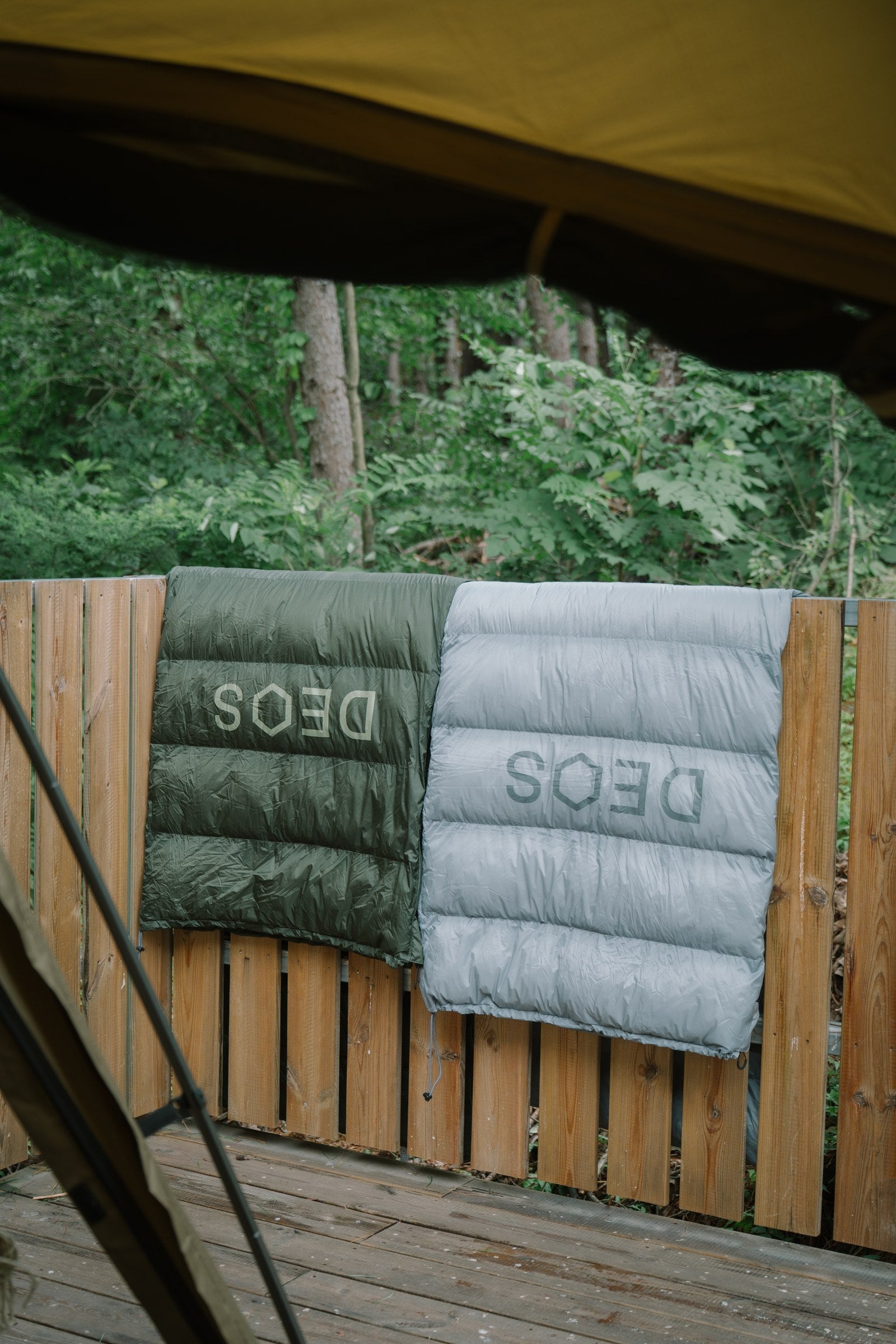 Olive and gray DEOS camp comforters airing on a deck rail in the forest