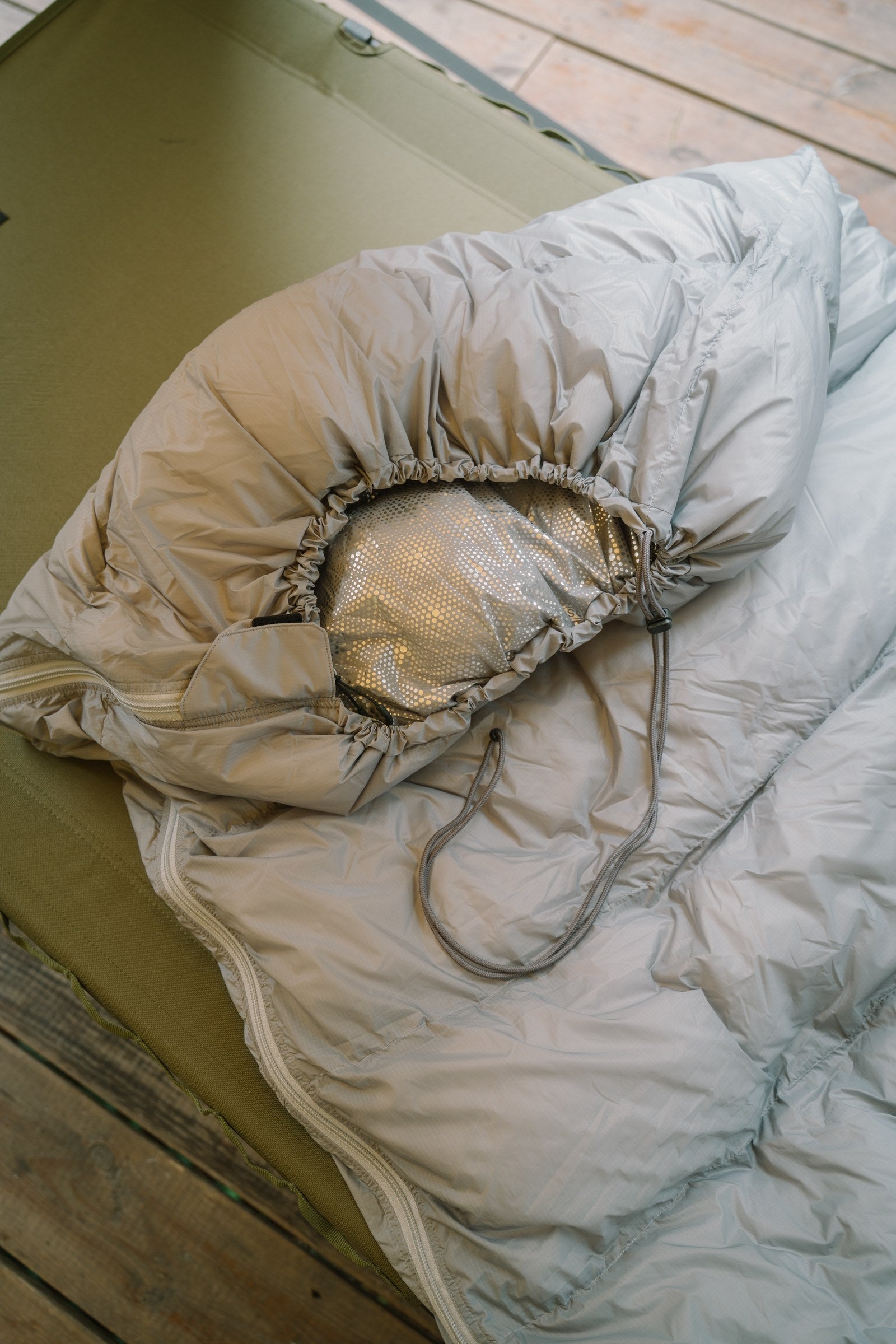 Gray DEOS camp comforter opened to show the heat-reflective lining inside a tent