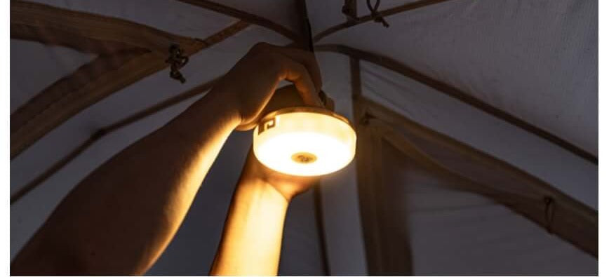 Hand holding the lit lantern up inside a tent, lighting the interior