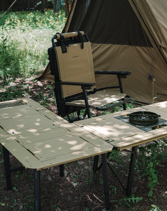 Tan FLOW folding chair with organizer in front of a tent with camp tables