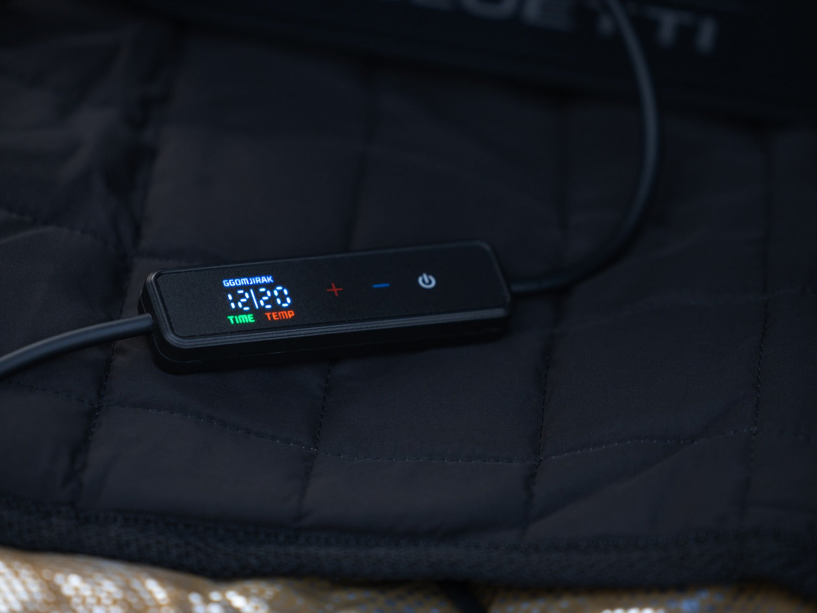 Close-up of the Carbon Heating Pad Large controller resting on the black quilted pad, its LED panel lit.
