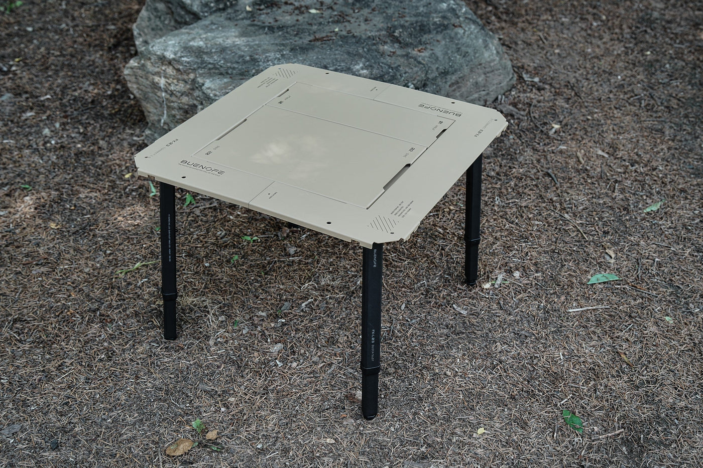 BUENOFE IGT Connect Table 1.5 assembled as a tan standalone table standing on a large rock in a shaded forest, shown at a three-quarter angle in natural daylight.