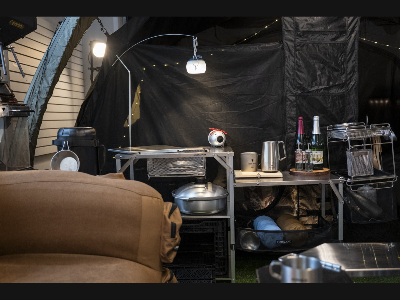 The lantern hanger mounted on a camp shelf at night, the lit lantern hanging over the work surface instead of standing on it.