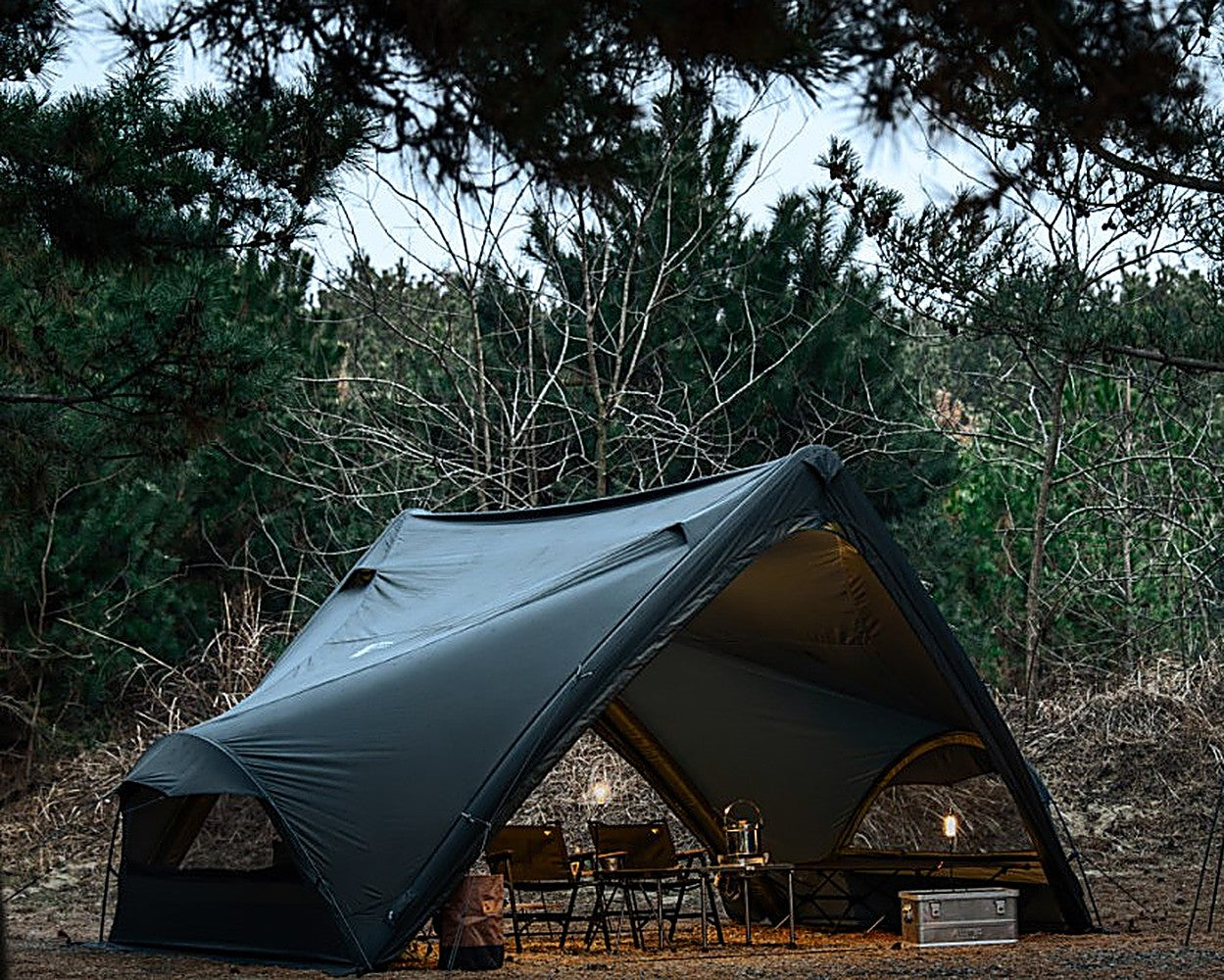 Super Position MGX-600 pitched in a pine forest at dusk, sheltering camp chairs and a lantern-lit table