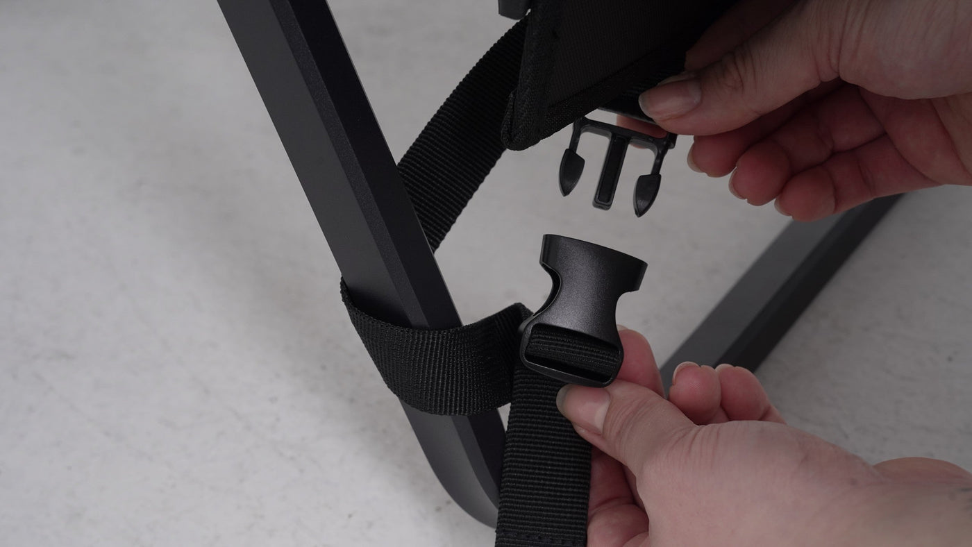 BUENOFE Multi Storage Bag Slim being fastened to the lower frame of a camp chair as hands connect the bottom strap buckle around the chair leg, completing the three-step mounting process.