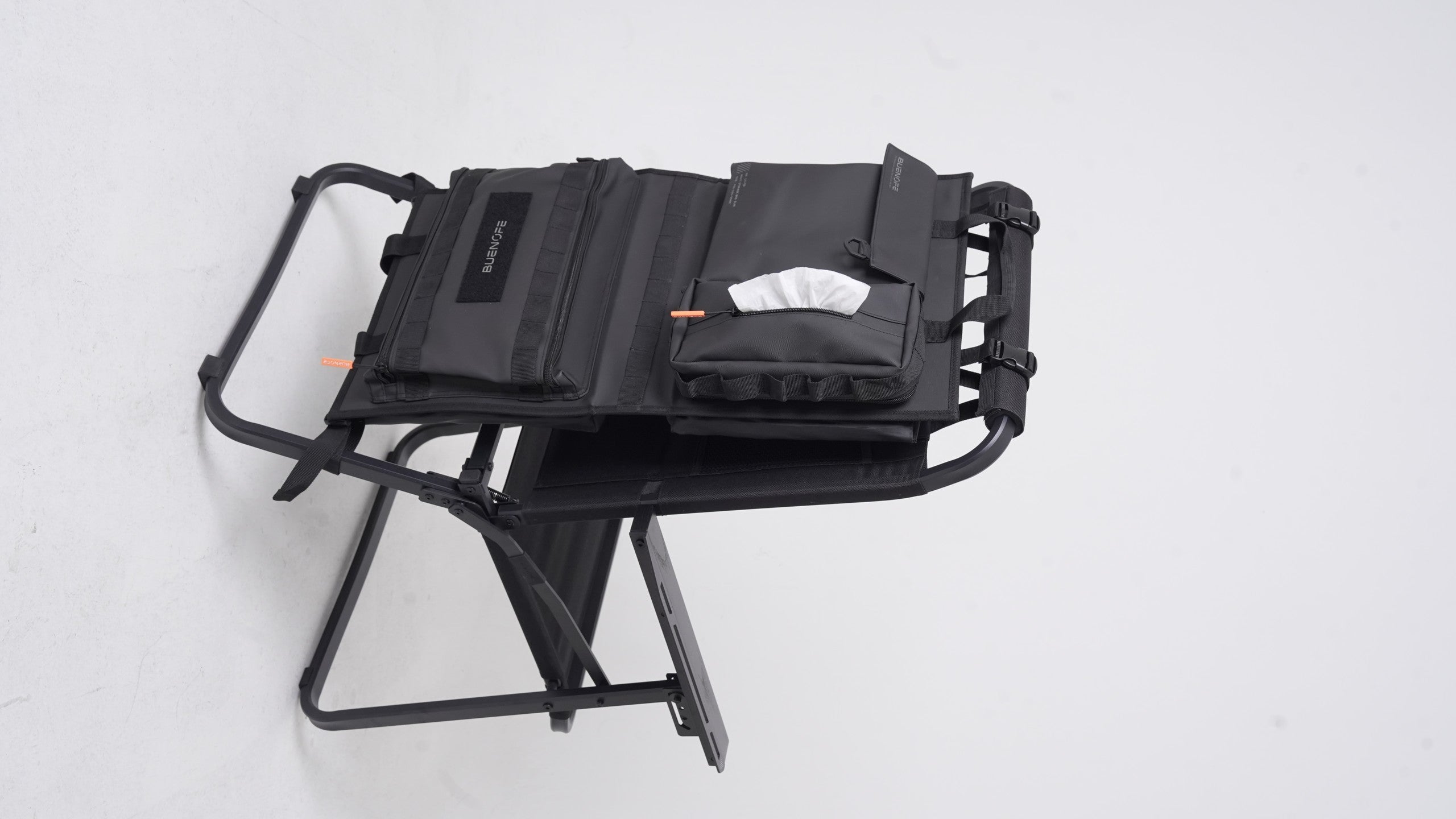 BUENOFE Multi Storage Bag Slim opened flat on a folded chair frame with the detachable tissue pouch dispensing a single white tissue through its center opening, showing the built-in tissue function at camp.