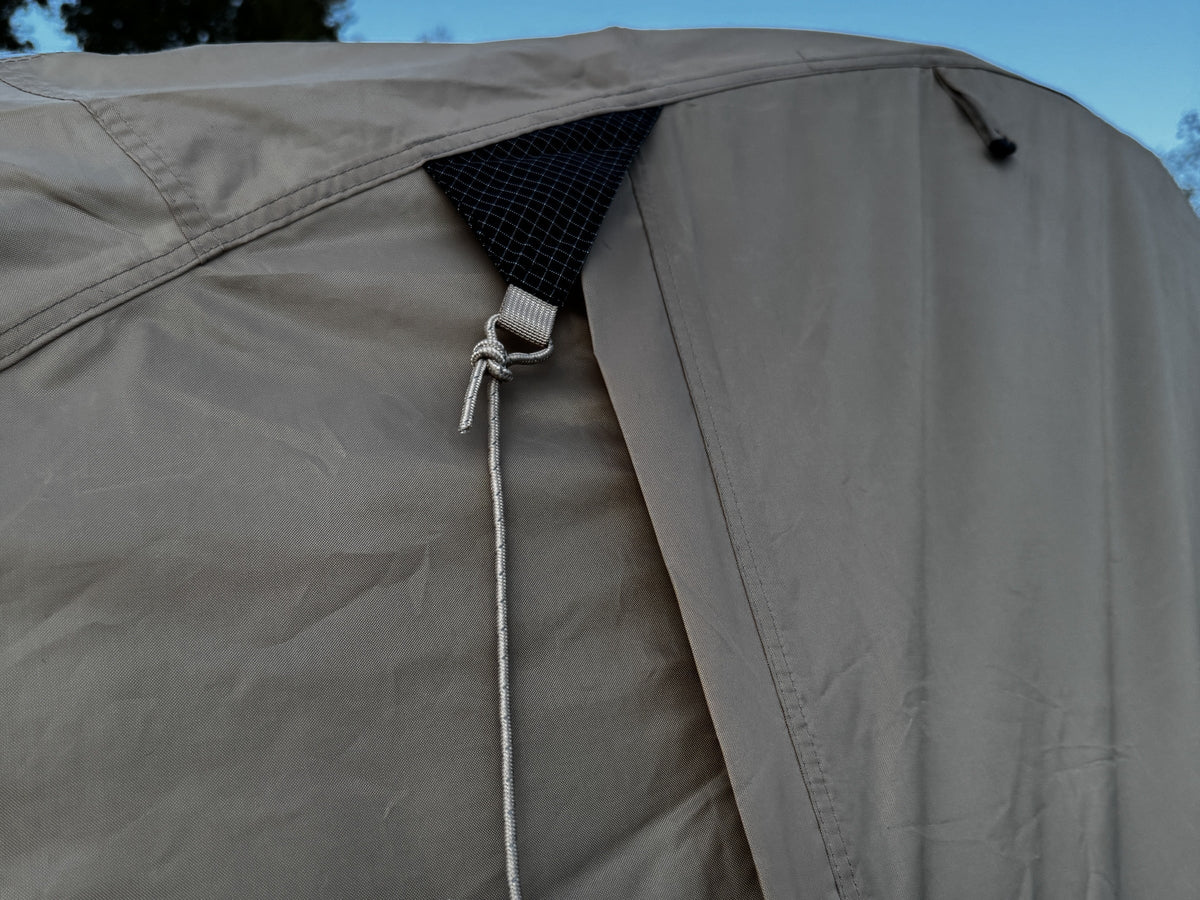 Guy line with tension hook coiled at a reinforced corner of the Natural rainfly.