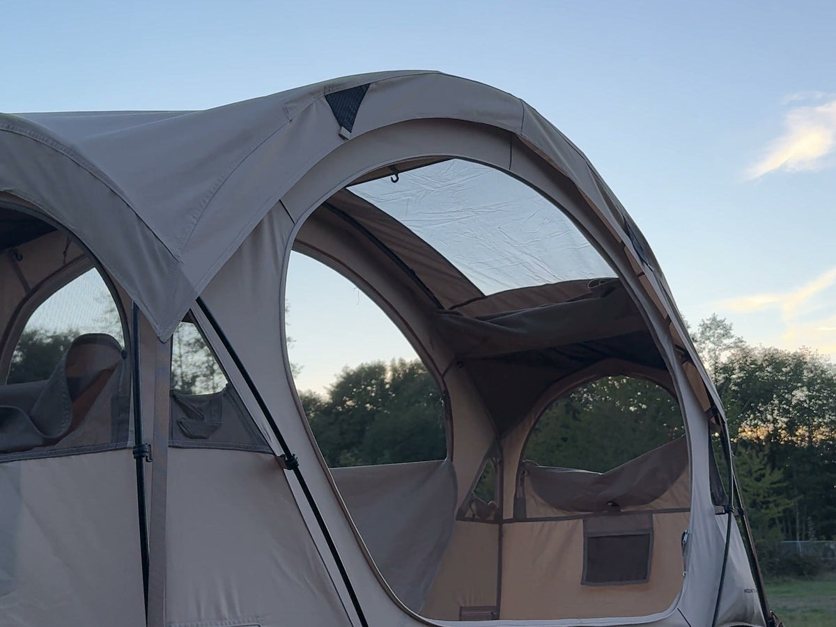 Neo Nest 80 at dusk with the included roof cover fitted over the arched roof, on a camp cot (cot sold separately).