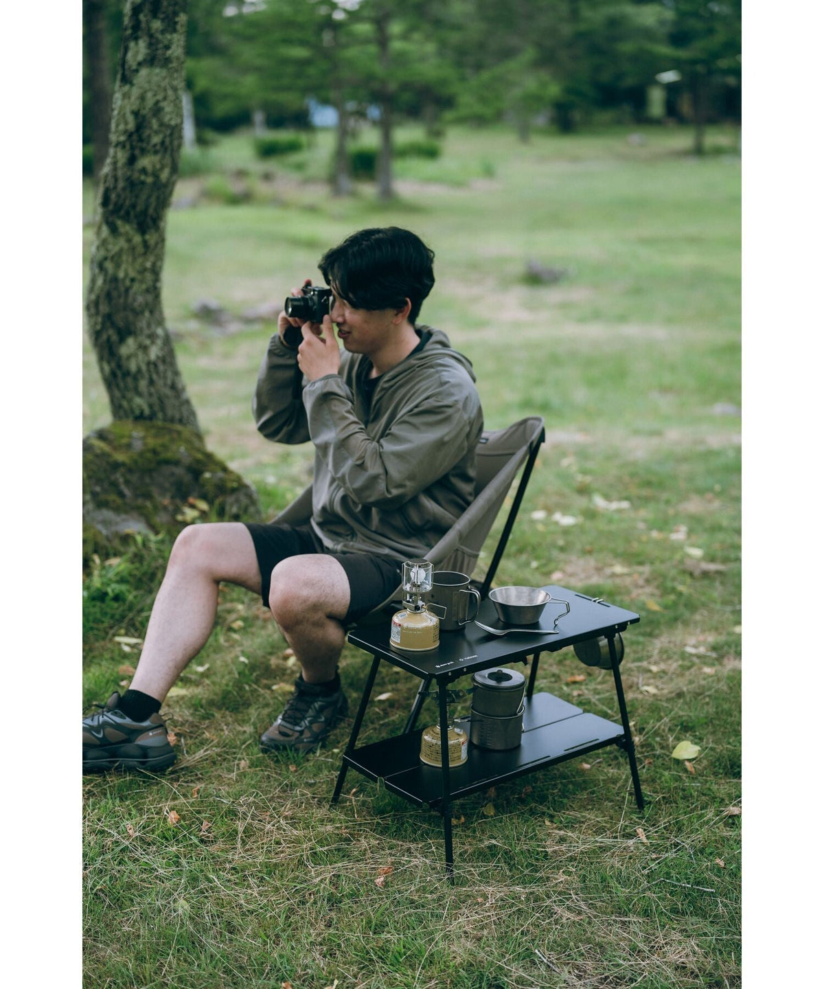 Noga Table, Black, beside a camp chair with a lantern on the lower shelf