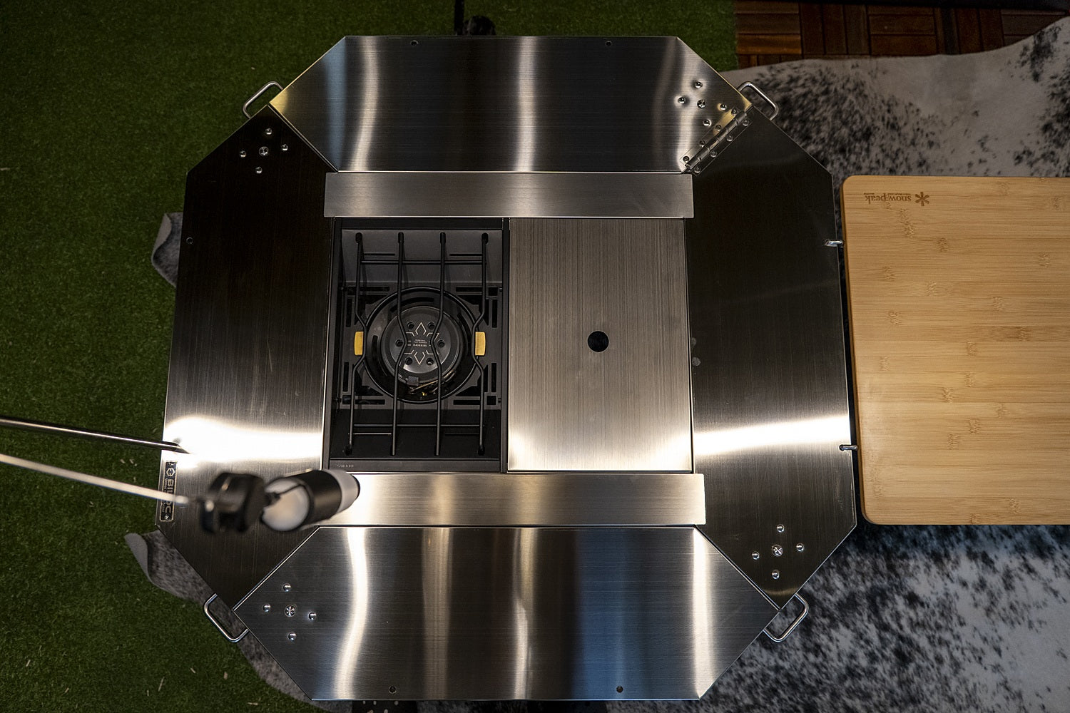 Octa table from above with the two-piece inner table set fitted and a burner in one bay, set up beside a side table. The burner, lantern and side table shown are not included.