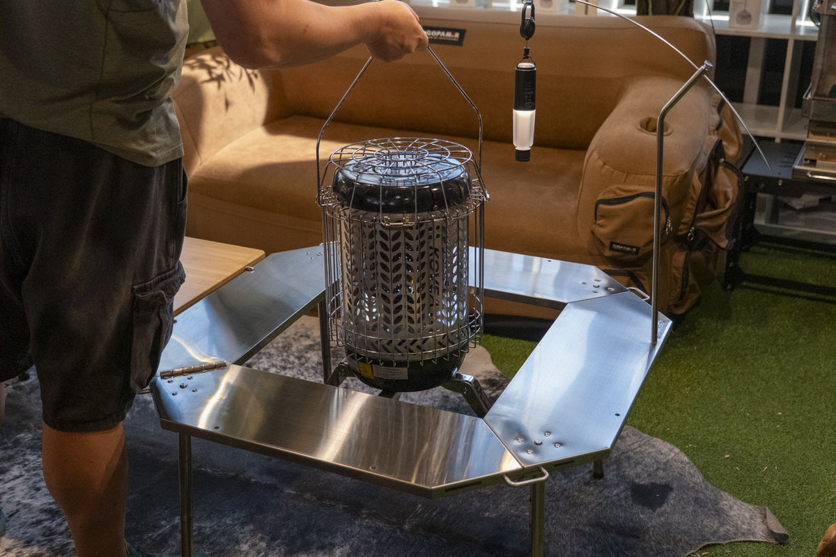 Caged gas heater being lifted by its bail handle into the open centre of the Biloc Octa table in a showroom. The heater, lantern and hanger shown are not included.