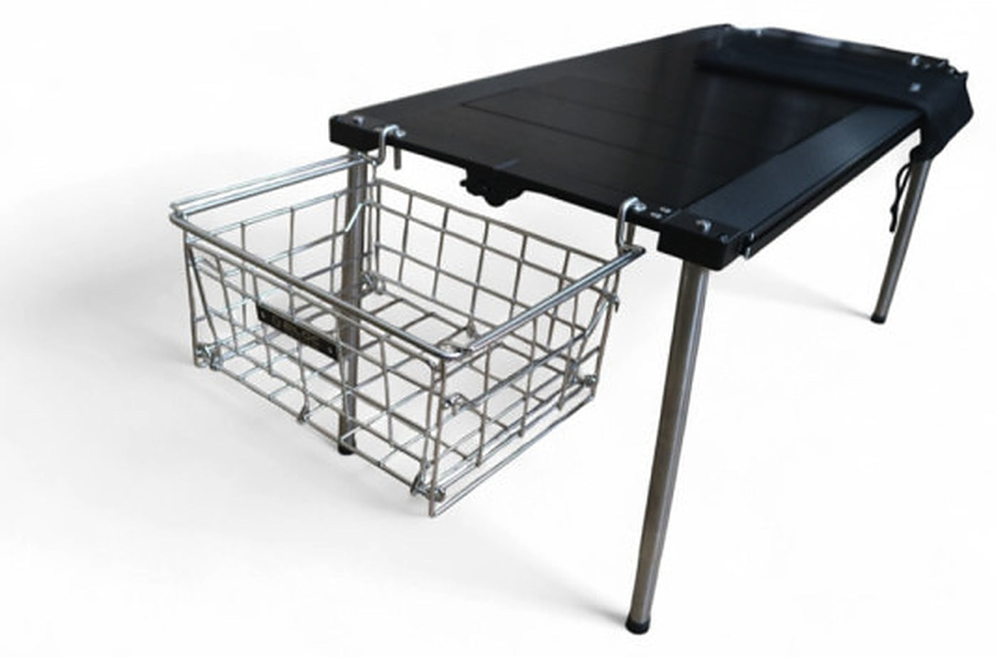 Wire basket hanging from a side hanger below a camp table edge. The basket is a separate purchase.