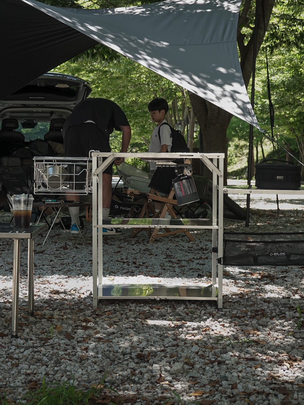 Biloc Stella IGT camp shelf standing under a tarp with cookware basket and mesh pocket