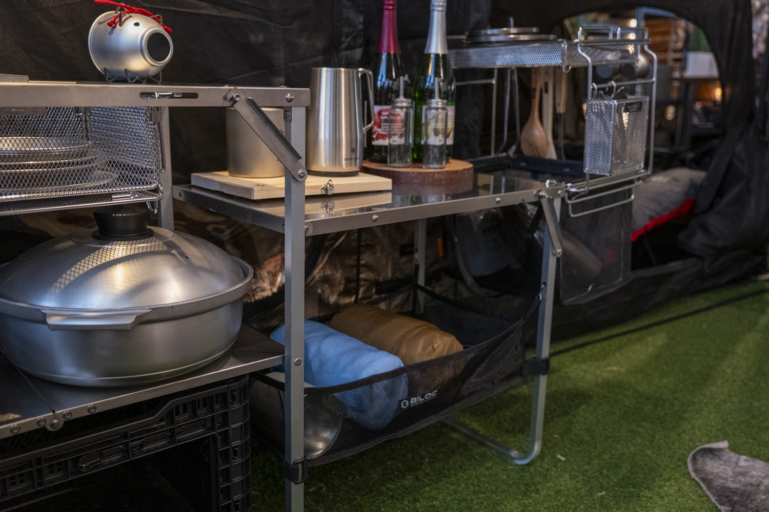Side view of the Stella shelf loaded: a wok on the mid tier and soft storage bags on the bottom shelf. The cookware shown is not included.