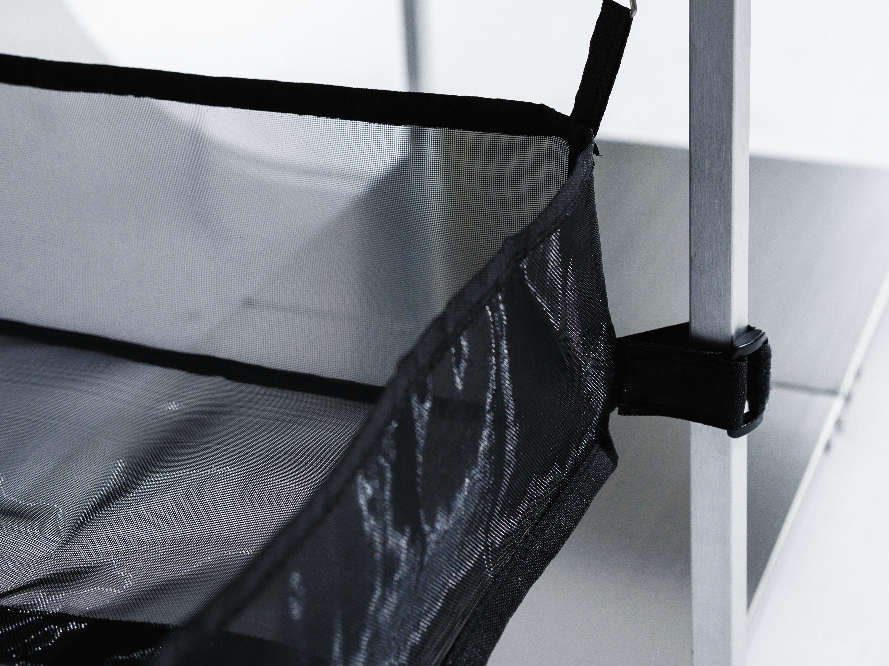 The included black mesh basket hooked by a wire hook under the side-table rail and secured to the leg with a hook-and-loop strap.